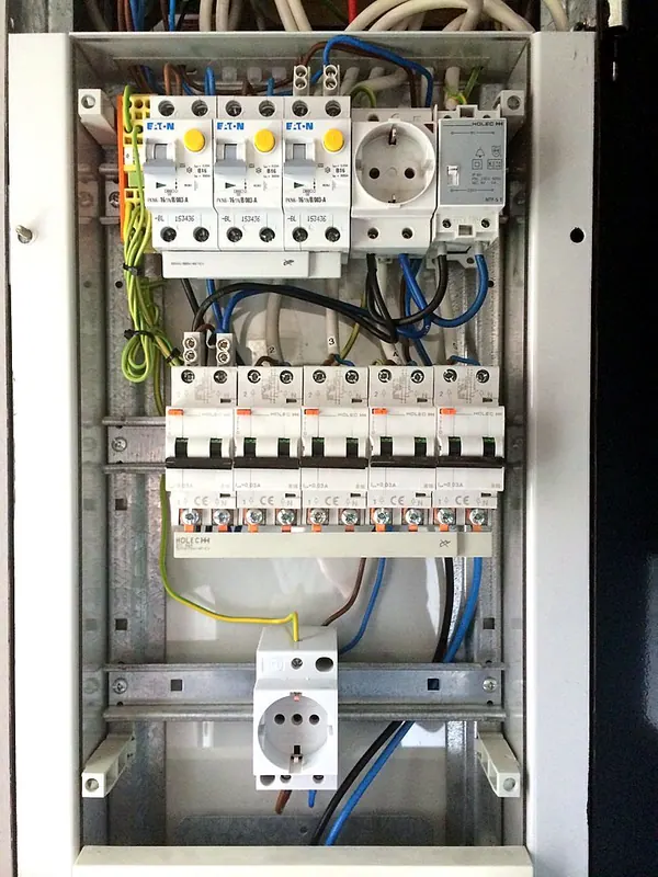 Open groepenkast met bovenin drie aardlekautomaten met gele testknop, een stopcontact en een beltransformator, in het midden vijf groepen en onderin een rail met een stopcontact en nog lege ruimte